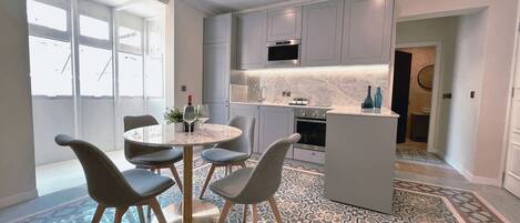 A modern kitchen with grey cabinets, a central island, and a dining area with a round table and chairs.