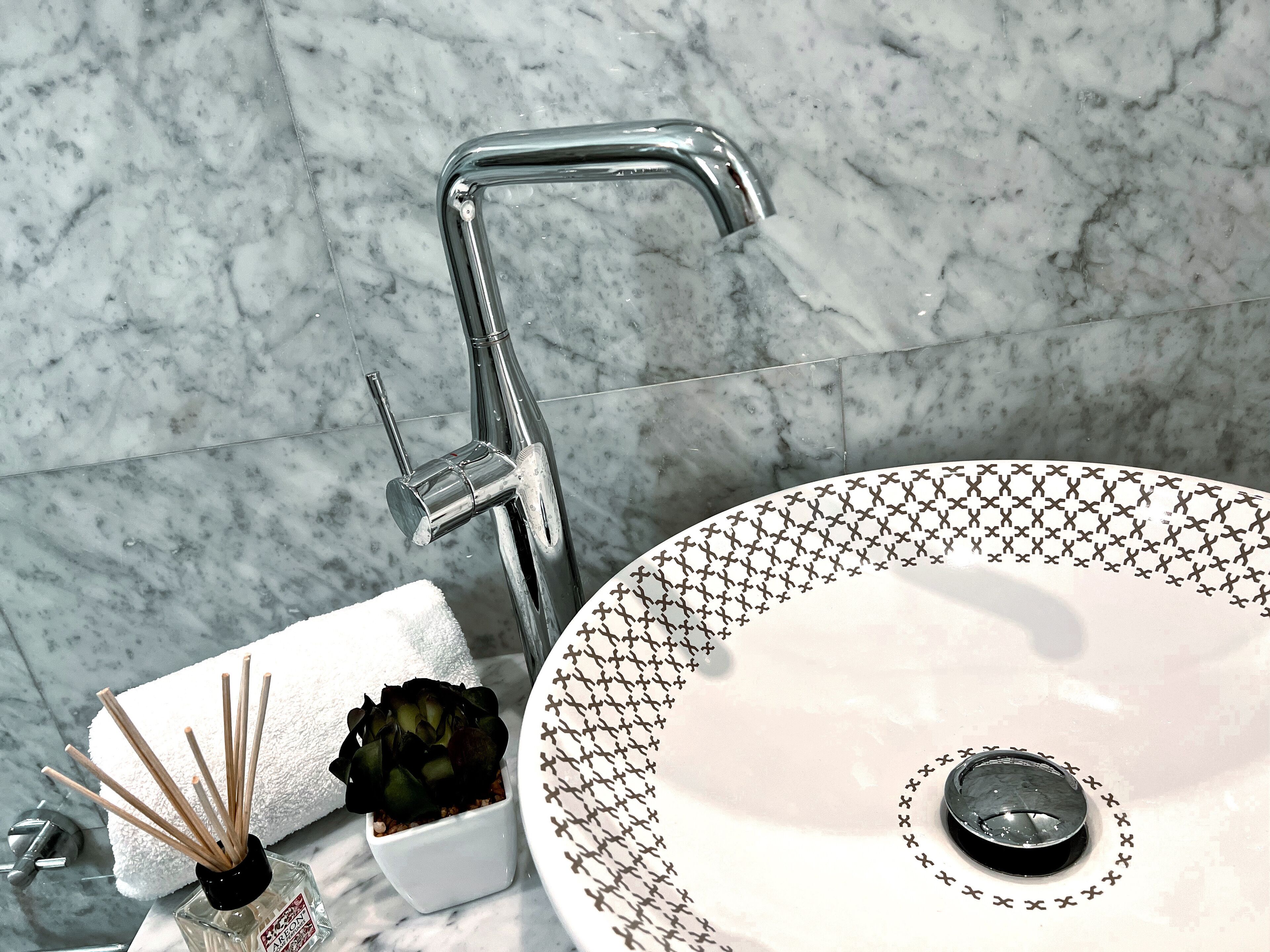 Ein Badezimmer mit Marmorwaschbecken, einem modernen Wasserhahn, einem Handtuch und einer kleinen Topfpflanze.