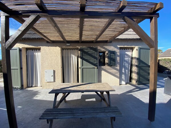 A wooden pergola with a table in front, a building with green shutters, and a clear sky. - Fisherman's Island Mas (Le Barcarès)