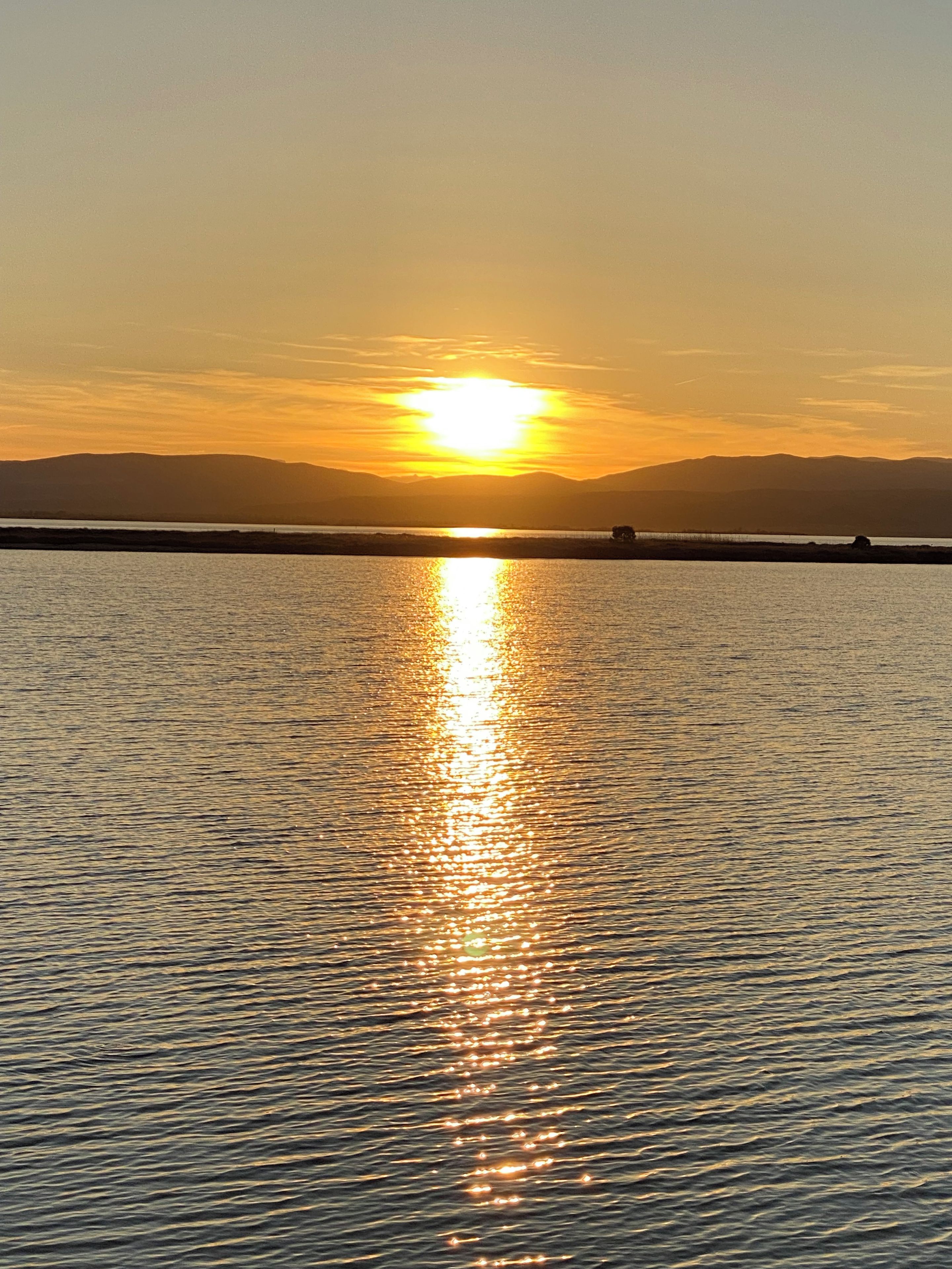 A sunset over a calm body of water with distant mountains.