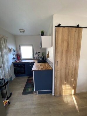 Une cuisine compacte dotée d’un plan de travail en bois, d’un four encastré et d’une porte coulissante.