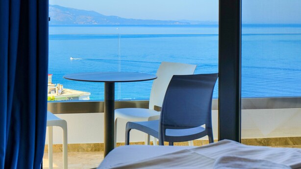 Un cuarto de hotel con una cama, una mesa y sillas, y vista al mar.