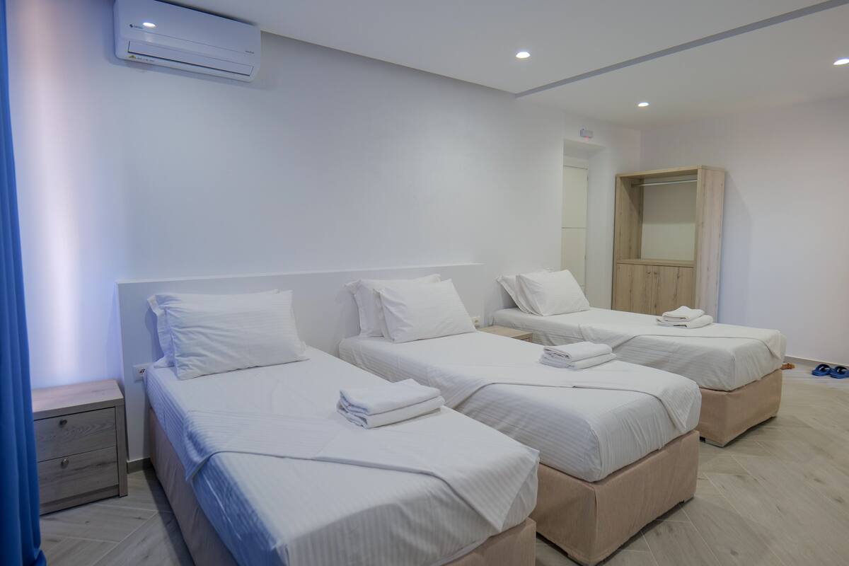 A hotel room with three single beds, a wooden wardrobe, and an air conditioning unit.