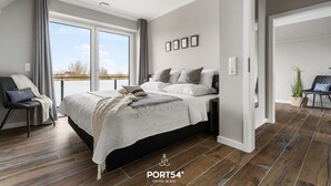 Quarto moderno com uma cama grande, uma cadeira e vista para o exterior.