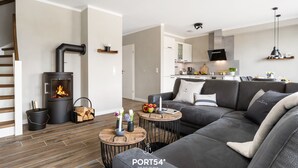 Uma sala de estar moderna com lareira, sofá cinzento, mesa de centro de madeira e cozinha ao fundo.