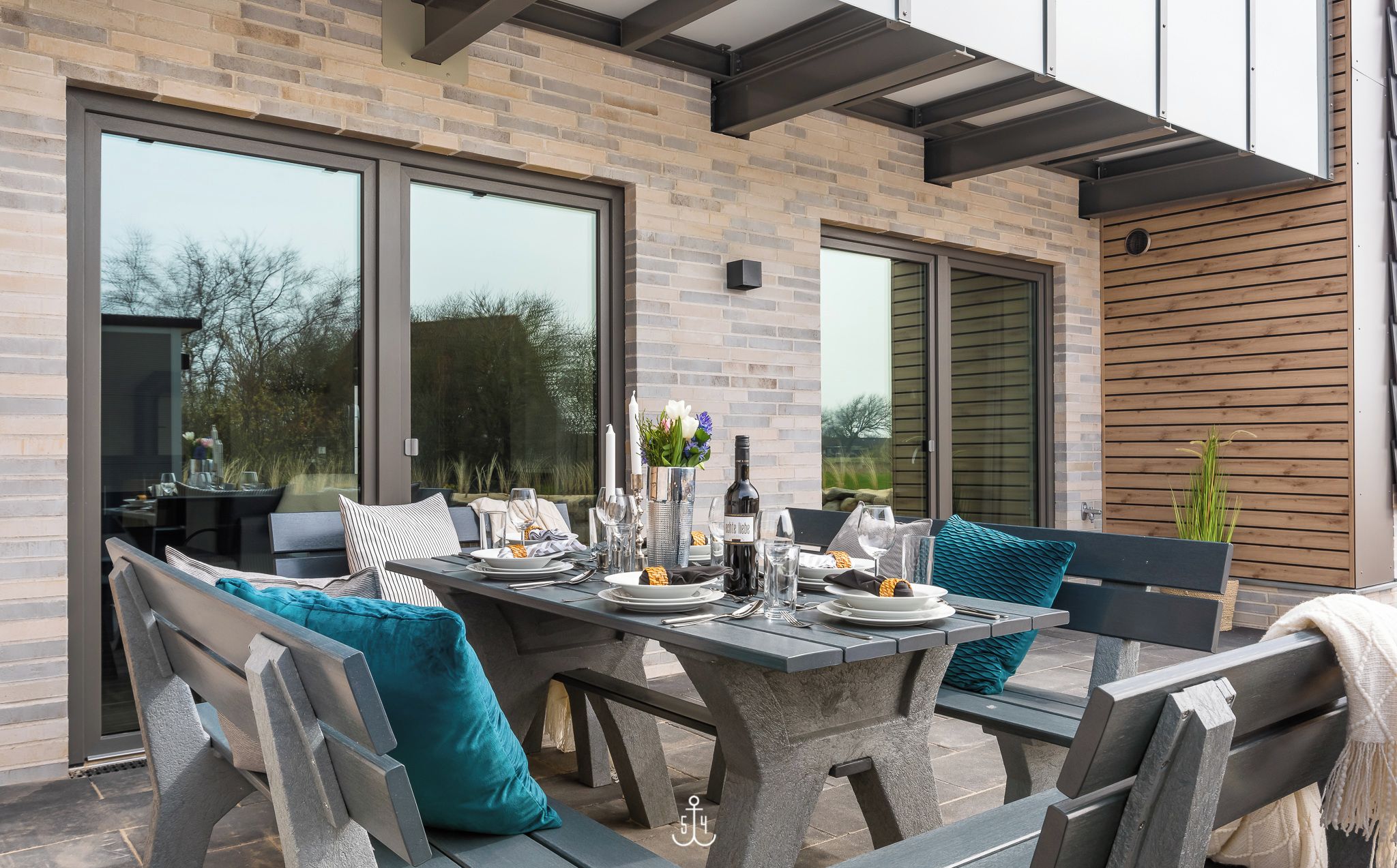 Un espace de restauration en plein air avec une table et des bancs en pierre, de grandes fenêtres et un mur en bois.