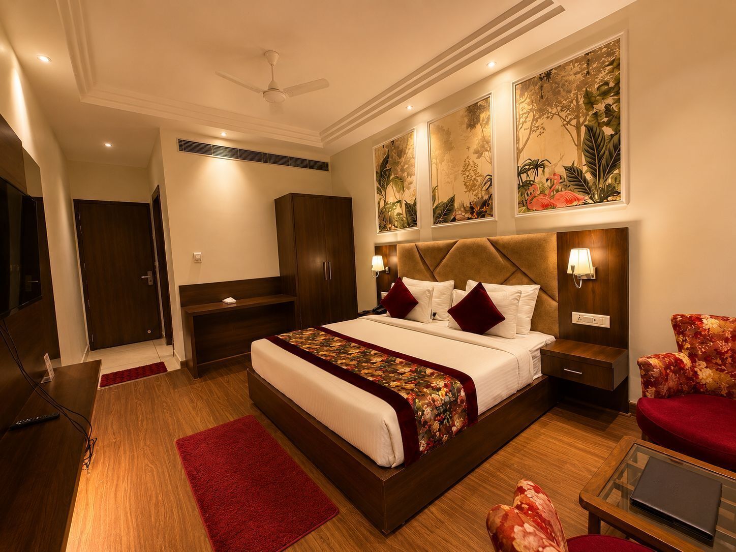 A hotel room with a large bed, a desk, a wardrobe, a TV, and artwork on the walls.