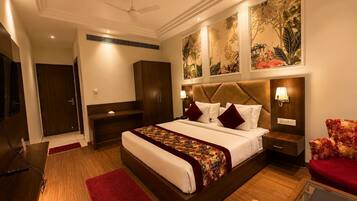 A hotel room with a large bed, a desk, a wardrobe, a TV, and artwork on the walls.