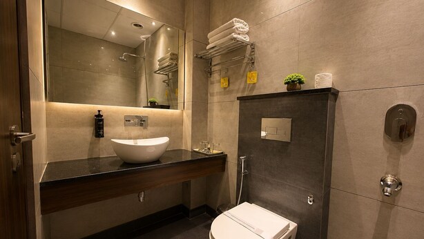 A modern bathroom with a large mirror, a white sink, a toilet, and a shower area.