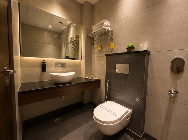 Un baño moderno con un espejo grande, un lavamanos blanco, un inodoro y una zona de ducha.