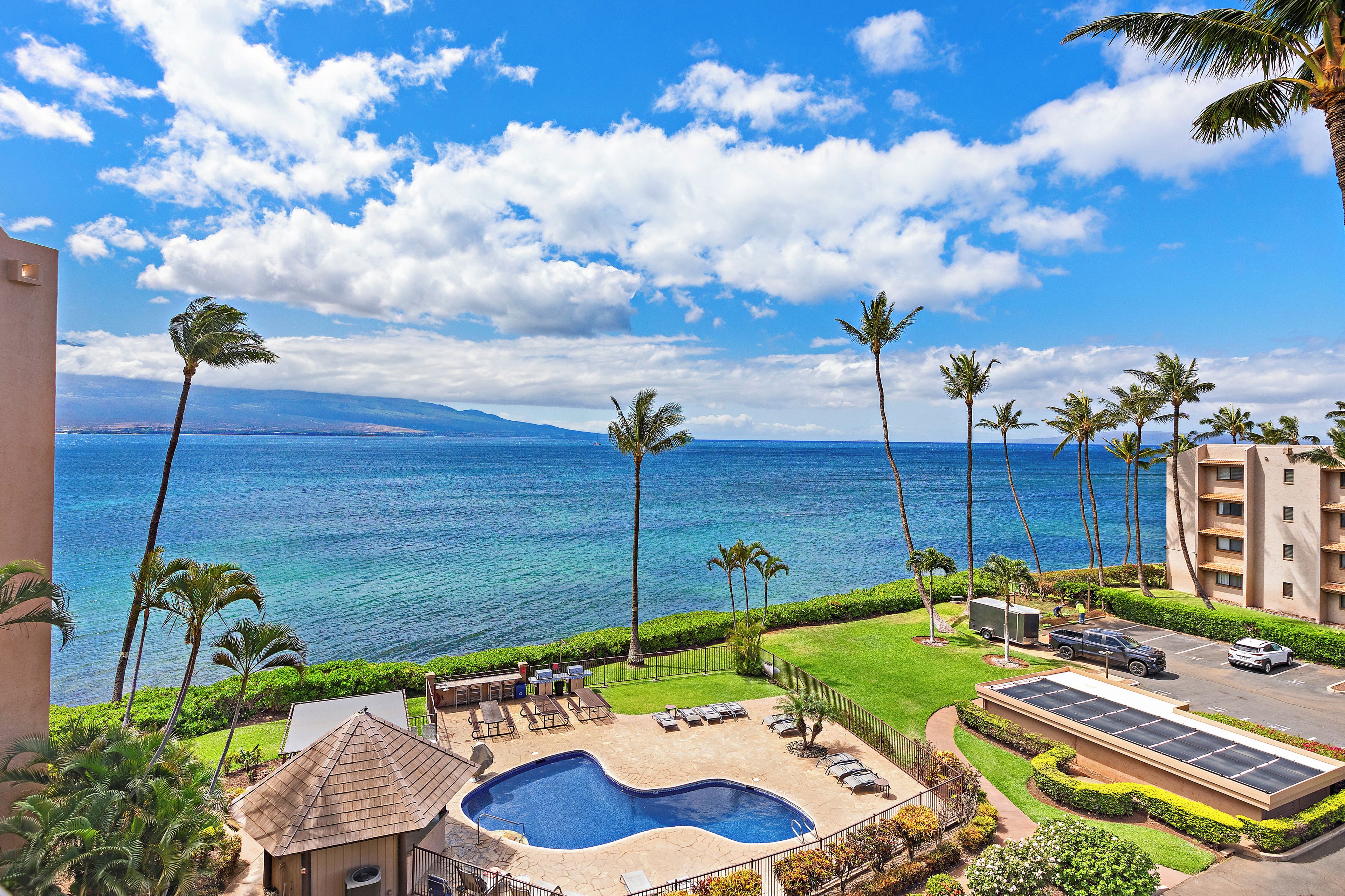 A pool area with a view of the ocean, surrounded by palm trees and a building with a balcony.