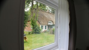 A window with a view of a thatched-roof house and a lawn. - Apartment "PASTORATSGARTEN SCHLEI": Relax and enjoy (Norderbrarup)