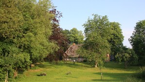 A rural landscape with a thatched-roof house surrounded by lush greenery. - Apartment "PASTORATSGARTEN SCHLEI": Relax and enjoy (Norderbrarup)