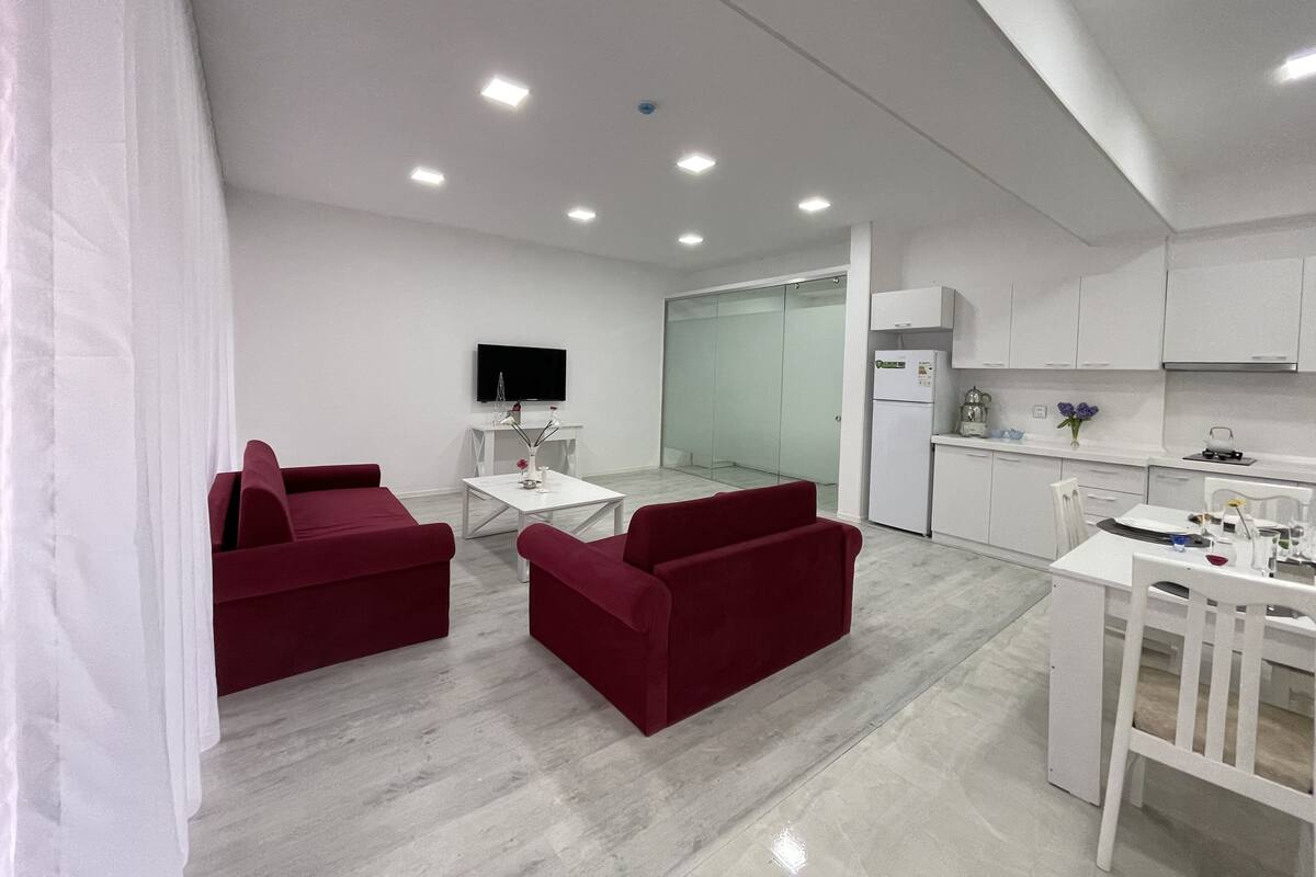 Un salon moderne avec des canapés rouges, une table basse blanche et un téléviseur à écran plat posé sur un meuble blanc.