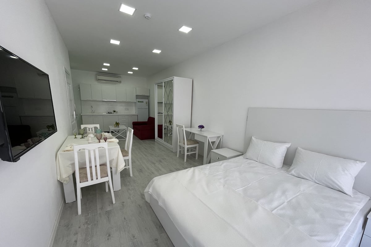 Une chambre d’hôtel moderne avec un grand lit, un coin repas comprenant une table et des chaises, et une petite cuisine en arrière-plan.