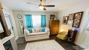 Un salon chaleureux avec un canapé, un fauteuil, un tapis, un ventilateur de plafond et un meuble contenant des objets décoratifs.