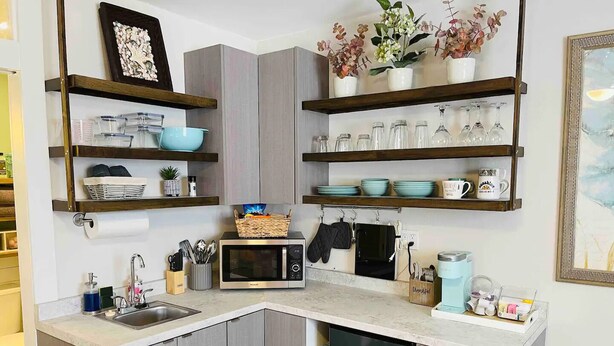 Une cuisine compacte dotée d’appareils électroménagers intégrés, d’étagères en bois et d’un petit réfrigérateur.