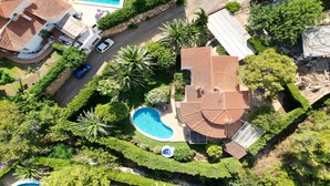 Vista aérea de una zona residencial con piscina rodeada de abundante vegetación y una casa con tejado de tejas.