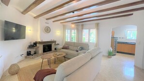 Sala de estar con sofá, chimenea, televisión y un área de cocina visible a través de un vano abierto.