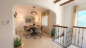 Un comedor con una mesa redonda y sillas, una lámpara en el techo y vistas al exterior a través de una ventana con cortinas.