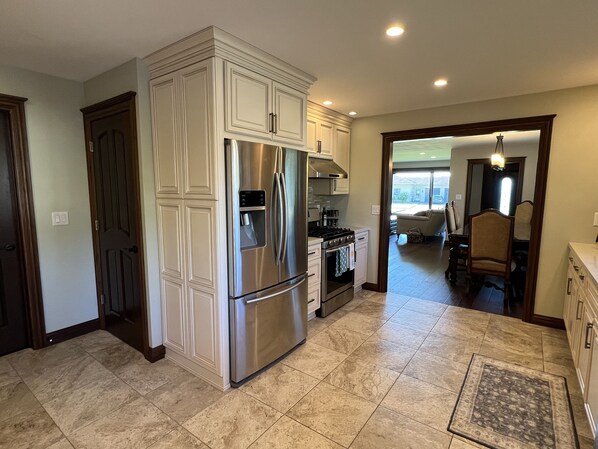 A spacious kitchen with a stainless steel refrigerator, oven, and gas stove. There is a large window providing natural light and a view of the outside.
