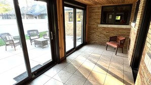 Un vaste espace intérieur doté d’un plafond en bois, de grandes portes-fenêtres coulissantes donnant sur une terrasse extérieure et d’un sol carrelé.