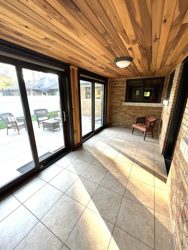 A spacious indoor area with a wooden ceiling, large sliding glass doors leading to an outdoor patio, and a tiled floor.