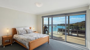 Quarto com cama, mesas de cabeceira e vista para uma varanda com piscina e paisagem.