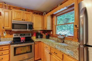 Una cocina con armarios de madera, electrodomésticos de acero inoxidable, un ventanal con vistas a la vegetación y una encimera de granito.