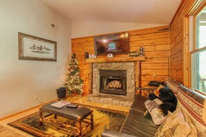 Una sala acogedora con chimenea de piedra, un televisor montado encima y un árbol de Navidad.