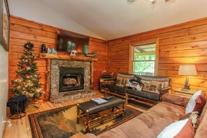 A cozy cabin interior with a stone fireplace, wooden walls, a Christmas tree, and a sofa.
