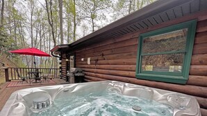 Eine Holzhütte mit Whirlpool auf einer Terrasse, umgeben von Bäumen.