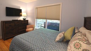 Un dormitorio con cama, cómoda, silla, televisor y ventana con persianas.