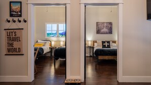 A hotel room with a wooden floor, a bed with a black and white pillow, a window with a view of a park, and a wall with a 'Let's Travel the World' sign.