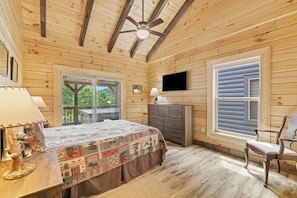 A bedroom with a bed, dresser, television, and a window with blinds.