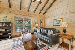 A cozy cabin interior with a leather sofa, wooden coffee table, and a bookshelf. - Magical Memories Brand New Veranda Level Cabin Overlooking Pond in Heart of Bryson City (Bryson City)