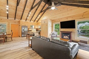 A cozy cabin interior with a wooden floor, a leather sofa, a dining area, and a fireplace. - Magical Memories Brand New Veranda Level Cabin Overlooking Pond in Heart of Bryson City (Bryson City)