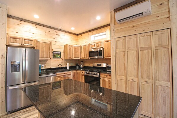 View of the kitchen showcasing granite surfaces, wood cabinetry, stainless appliances, and laundry area. Well-equipped cabin rental in Bryson City.