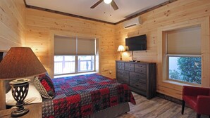 Ein Schlafzimmer einer Holzhütte mit Bett, Schminktisch, Fernseher und Fenstern.