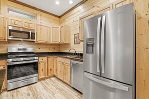 A modern kitchen with wooden cabinetry, stainless steel appliances including a refrigerator, oven, and microwave, and a granite countertop.