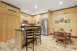A kitchen with wooden cabinets, a microwave, a stove, a refrigerator, and a dining area with chairs and a table. - Huggie Bear Located in Bryson Village in Town. Pet Friendly! (Bryson City)