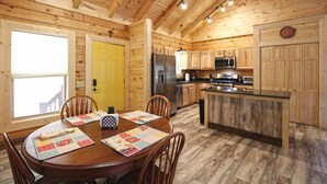 A wooden cabin interior with a dining area, kitchen, and a yellow door. - Moose Tracks Downtown Veranda Level Cabin with Hot Tub (Bryson City)
