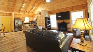 A cozy log cabin interior with a living room, kitchen, and fireplace. - Moose Tracks Downtown Veranda Level Cabin with Hot Tub (Bryson City)