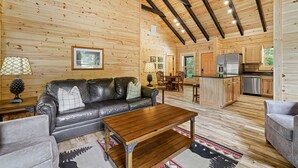Interior de una cabaña de madera con sala de estar, comedor y cocina.
