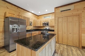 Eine Küche mit Holzschränken, einem Edelstahlkühlschrank, einer Mikrowelle, einem Herd und Arbeitsplatten aus Granit.