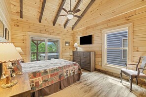 Une chambre dans une cabane en bois, avec un lit, une commode, une télévision et une grande fenêtre.