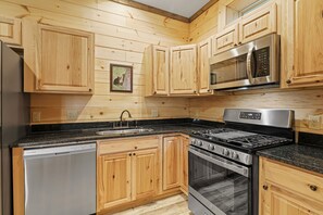 Eine Küche mit Holzschränken, einem Edelstahl-Kühlschrank, einer Spülmaschine, einer Mikrowelle und einem Herd.
