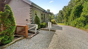 A log cabin with a gravel driveway, wooden deck, and a covered porch.