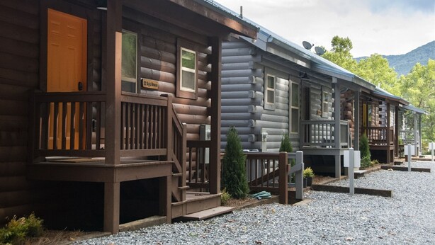 A row of log cabins with wooden decks and small steps leading to the entrance.