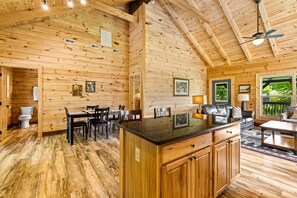 L’intérieur d’un chalet en bois comprend un coin repas, une cuisine et une grande fenêtre donnant sur un paysage verdoyant.